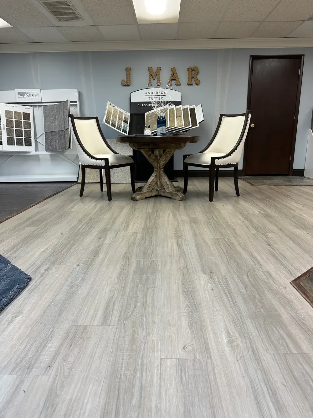 The J-Mar showroom floor, with "J MAR" wall lettering above sample racks from Shaw Floors and Anderson Tuftex