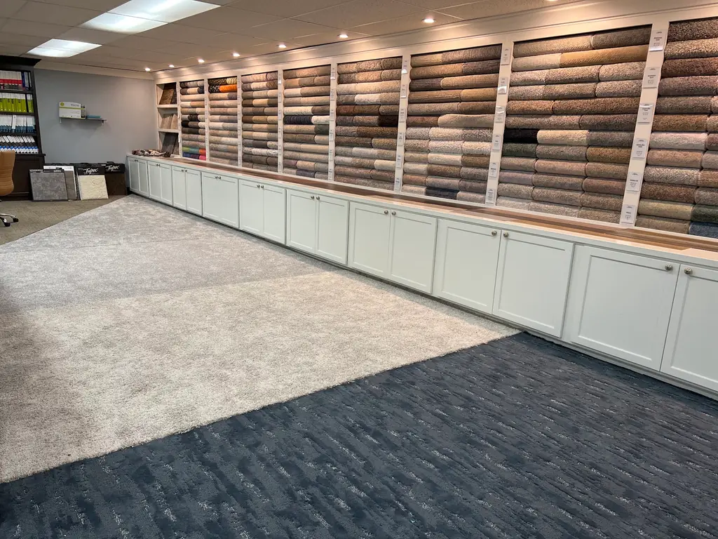 The carpet roll wall in the J-Mar showroom, lit shelving stacked with rolled samples above a run of cabinets